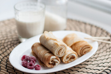 pancakes rolled up on a white plate with frozen raspberries on a wicker napkin