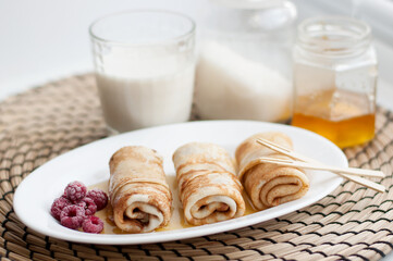 rolled pancakes drizzled with honey and frozen raspberries on a white plate on a wicker napkin