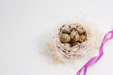 quail eggs in paper filling next to a pink satin ribbon on a white background