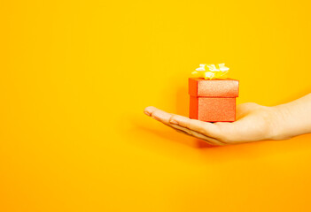 The girl's hand is holding a beautiful gift box. Makes a gift. Yellow background.