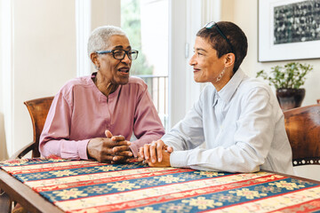 Elderly woman talks with her adult daughter sitting at a table at home