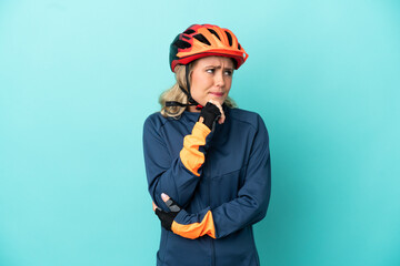 Young cyclist woman isolated on blue background having doubts and thinking