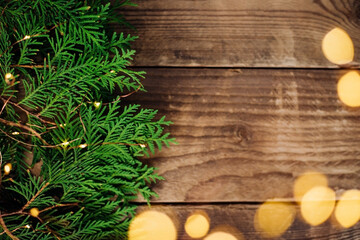 Background of Christmas lights of green thuja branches. Festive shiny garland and branches on the surface of wooden boards.