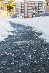 Winter road with salt for melting snow and apartment building in background. Selective focus