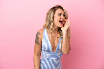 Young Brazilian woman in swimsuit in summer holidays isolated on pink background shouting with mouth wide open to the side