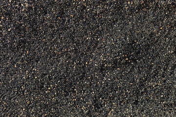 Black volcanic sand with rare grains of ordinary sand, top view. Texture or background