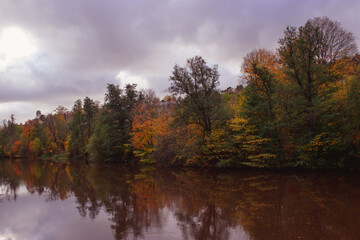 Fototapeta premium River lined with colorful trees in autumn, reflecting in the water.