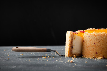 cheesecake with yellow mango flavoured layer decorated with red crumbs of freeze-dried raspberries. Cake cut on the dark marble background. Close up shot