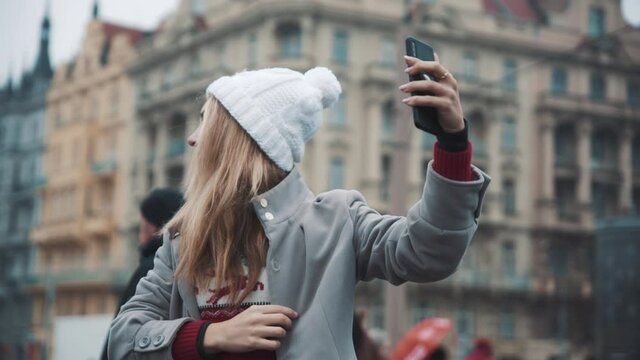 Pretty white woman taking selfie on phone on city background. Travel, happiness, xmas, holiday concept. Filmed on RED camera, 10 bit clolor