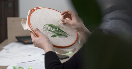 A woman is embroidering with a cross at a work table on which crumpled pieces of paper are scattered. A break during work.