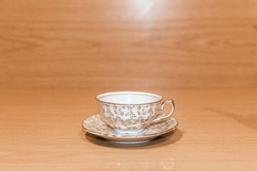 Pequeña taza de té y plato con adornos dorados sobre un fondo de madera