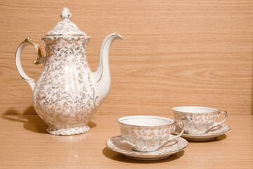 Juego de té con adornos dorados, dos pequeñas tazas de té con platos y tetera sobre un fondo de madera