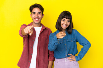 Obraz premium Young mixed race couple isolated on yellow background points finger at you with a confident expression