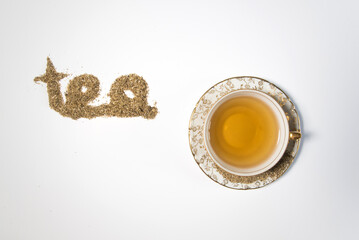 Vista cenital de una pequeña taza de té con adornos dorados sobre un fondo blanco. Hierbas secas...