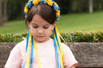 Little redhead preschooler girl with pigtails in national ukrainian folk decoration wreath outdoors