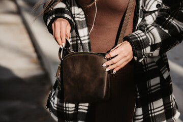 Outdoor fashion portrait of young fashionable girl wearing trendy checkered shirt, solid long sleeve bodycon one piece jumpsuits holding small brown color small bag