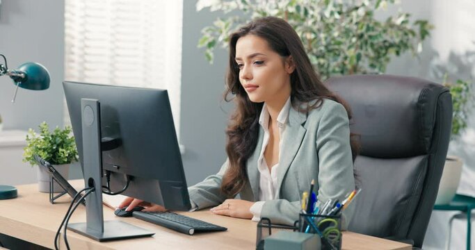 Pretty hard-working secretary of company assistant to boss manager sits at desk in office in front of computer screen tapping fingers on keyboard writing e-mails to clients sending documents projects