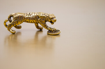 A bronze figure of a tiger with a coin - the symbol of the Chinese new year 2022 on a golden background, copy space. Wishes of good luck, financial well-being and wealth