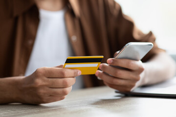 Yellow credit card and modern mobile phone in male hands