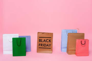 multicolored shopping bags and black friday lettering on pink background.