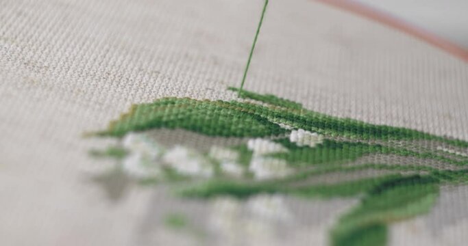 A man is embroidering with a cross on the canvas with green floss threads. Close-up.