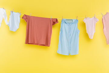 different clothes hanging on rope on yellow background.