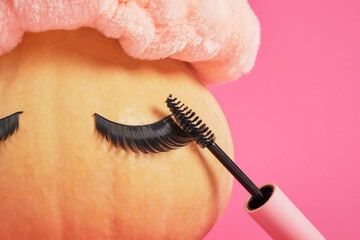 mascara in mock up blank pink packaging and pumpkin with false eyelashes on pink background copy space
