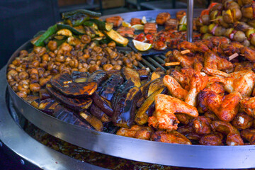 Street food. Assorted food grilled on a stainless steel turntable. Sausages, meat, corn, grilled vegetables. A slide of food. Large assortment of food grilling on a barbecue