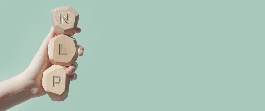 Letters NLP written on wooden irregular blocks hold by hand. Neuro-linguistic programming concept banner.