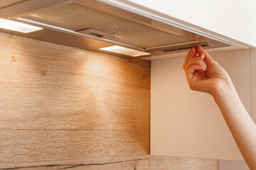 Woman hand turn on embedded cooker hood in white modern kitchen