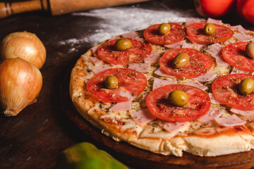 A pizza with lots of cheese, tomato, oregano and olives on a wooden table.