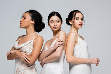 Young interracial women in satin dresses posing isolated on grey