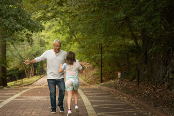 Fototapeta premium Father or grandfather with gray hair running and playing with younger girl on brick tree lined road