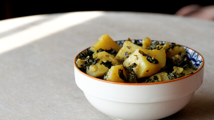 Fried dish with potatoes and kale leaves in bowl. Indian vegetarian cuisine Subji meal.