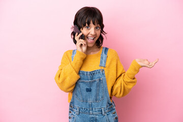 Young woman with overalls isolated background keeping a conversation with the mobile phone with someone