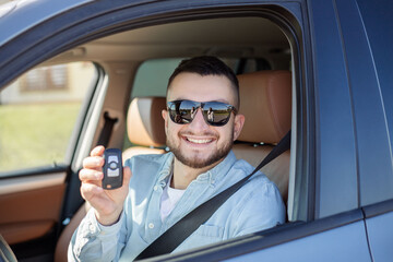 portrait of successful young happy man showing the keys sitting in new car.