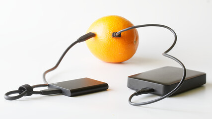External HDD and external SSD are connected to fresh orange. Concept of green technologies, data storage and transmission. White background. Solid State Drive and Hard Disk Drive