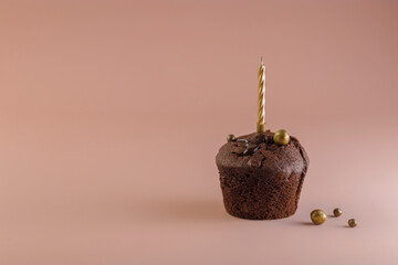 Chocolate muffin with a candle of gold color on a pink background. Holiday concept. Happy birthday card, happy anniversary. Minimalism