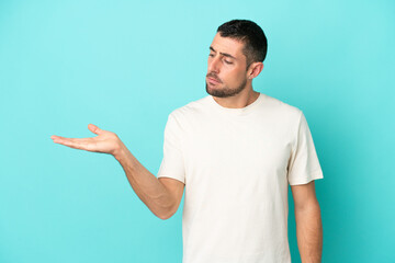 Young handsome caucasian man isolated on blue background holding copyspace with doubts