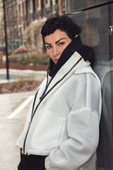 Stylish girl in a light jacket, with a calm and confident look, posing against the wall