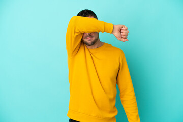 Young handsome caucasian man isolated on blue background covering eyes by hands