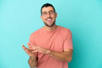 Young handsome caucasian man isolated on blue background With glasses and applauding