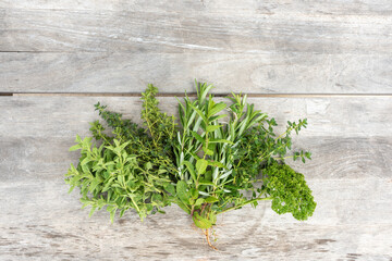 High angle view of freshly picked herbs on rough wooden table, including parsley, oregano, thyme and rosemary, with copy space