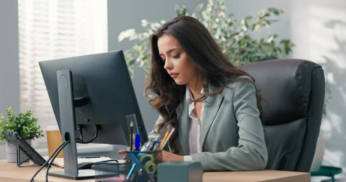Beautiful busy businesswoman sits at desk in front of computer in office, has technical problems with monitor, wrong screen setting, no signal, error, keyboard not working
