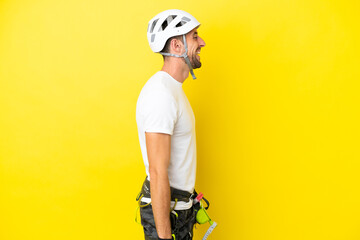 Young rock- climber man isolated on yellow background laughing in lateral position