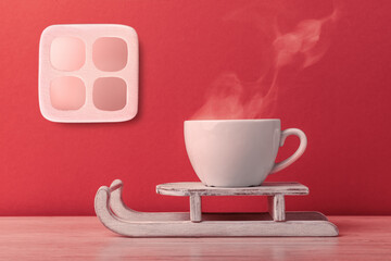Steaming cup of coffee on toy sleigh over red wall with window