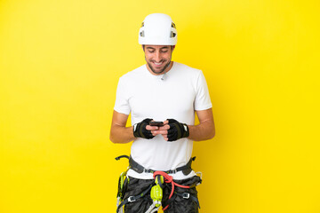 Young rock- climber man isolated on yellow background sending a message with the mobile