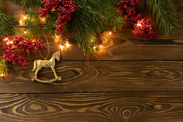 Christmas background. Nobilis fir branches, twigs with red berries, toy golden horse on brown wooden planks. Copy space, flat lay, top view. Holiday, Xmas, New Year concept. Mockup