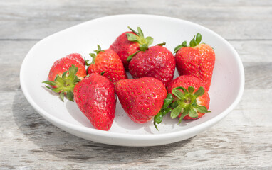 Close up of bright red srawberries in ceramic dish on rough wooden table (selective focus)