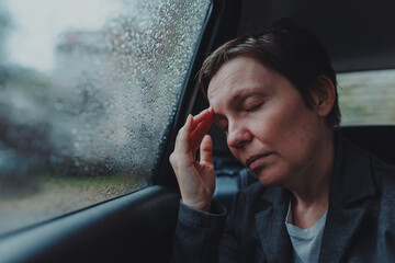 Businesswoman with severe headache sitting at the backseat of a car during rain
